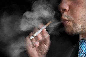 Young man (smoker) holds cigarette and smoking. A lot of smoke around.