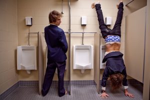Man looking to an other man pissing upside down in a restroom