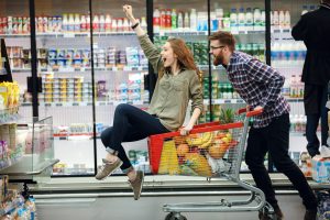 happy man pushing shopping cart with his girfriend inside at supermarket