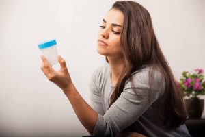 woman looking frustrated at a specimen cup she need to fill up