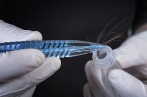 Forensic Scientist examining hair with sample vile.