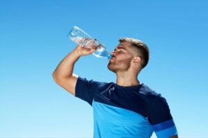 A man drinking water from a bottle against a blue sky background