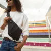 Person wearing a black crossbody sling bag over a white sweatshirt while standing on colorful outdoor stairs.
