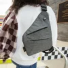 Person wearing a gray crossbody sling bag with diagonal zippered pockets and adjustable strap over a white sweatshirt.